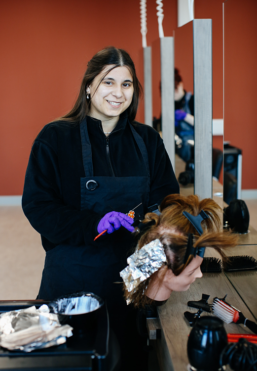 Student smiling whilst colouring hair on a mannequin