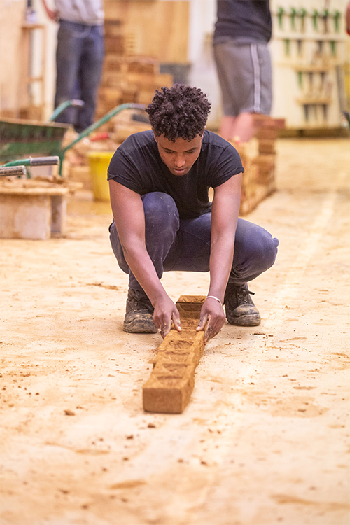 Student laying bricks beginning a brick wall