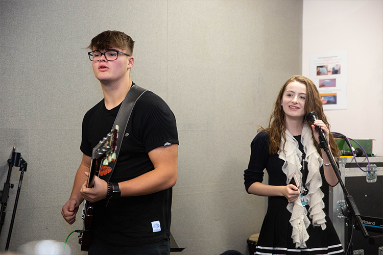 Student playing guitar with another student singing