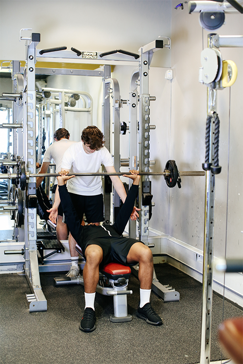 Two students weightlifting on a bench