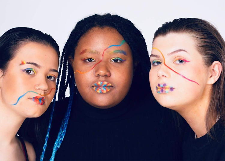 Three students with colourful makeup looking directly at camera