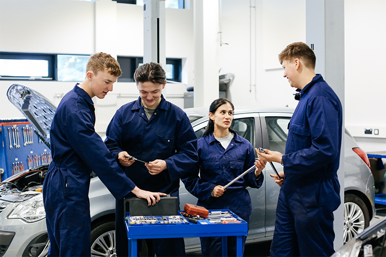 Four students chatting while fixing a car