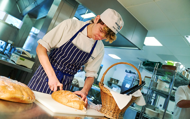 Professional cookery student slicing bread loaf