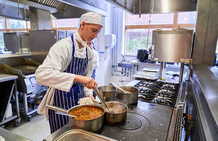 Professional cookery student stirring pots