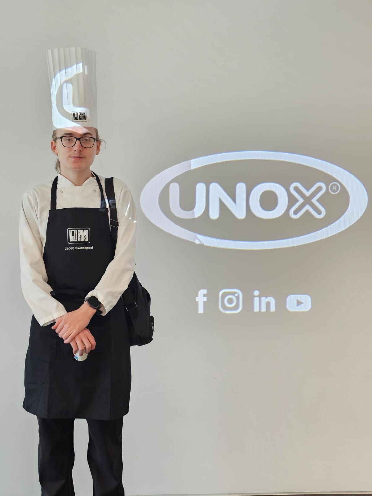 Jacob stood in chef whites in front of the UNOX sign