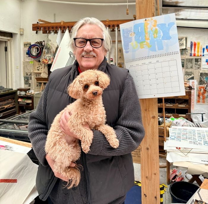 Alan Kitching smiling at camera holding dog infront of the calendar