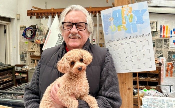 Alan Kitching smiling at camera holding a dog stood in front of the calendar