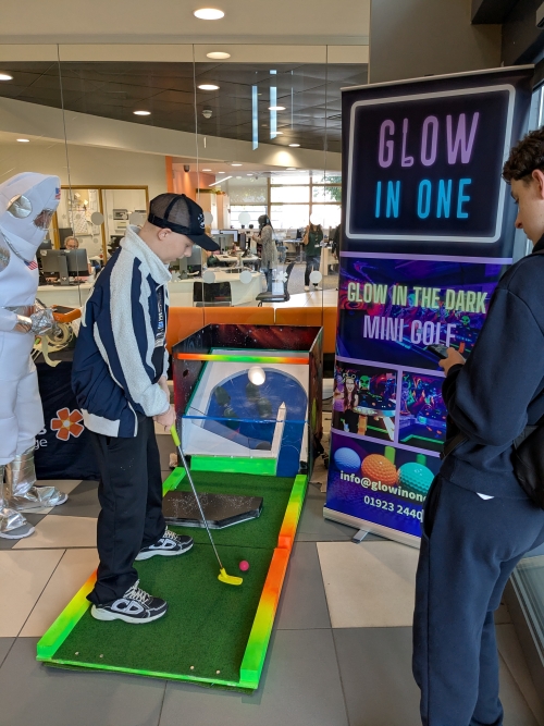 Student hitting a golf ball with a golf putt on a Glow In One branded mini-golf course