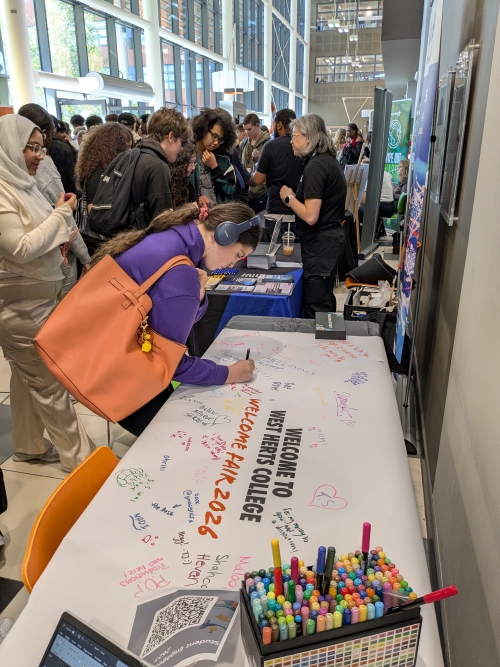 Student writing with a pen on a poster that is on a table about a welcome to college